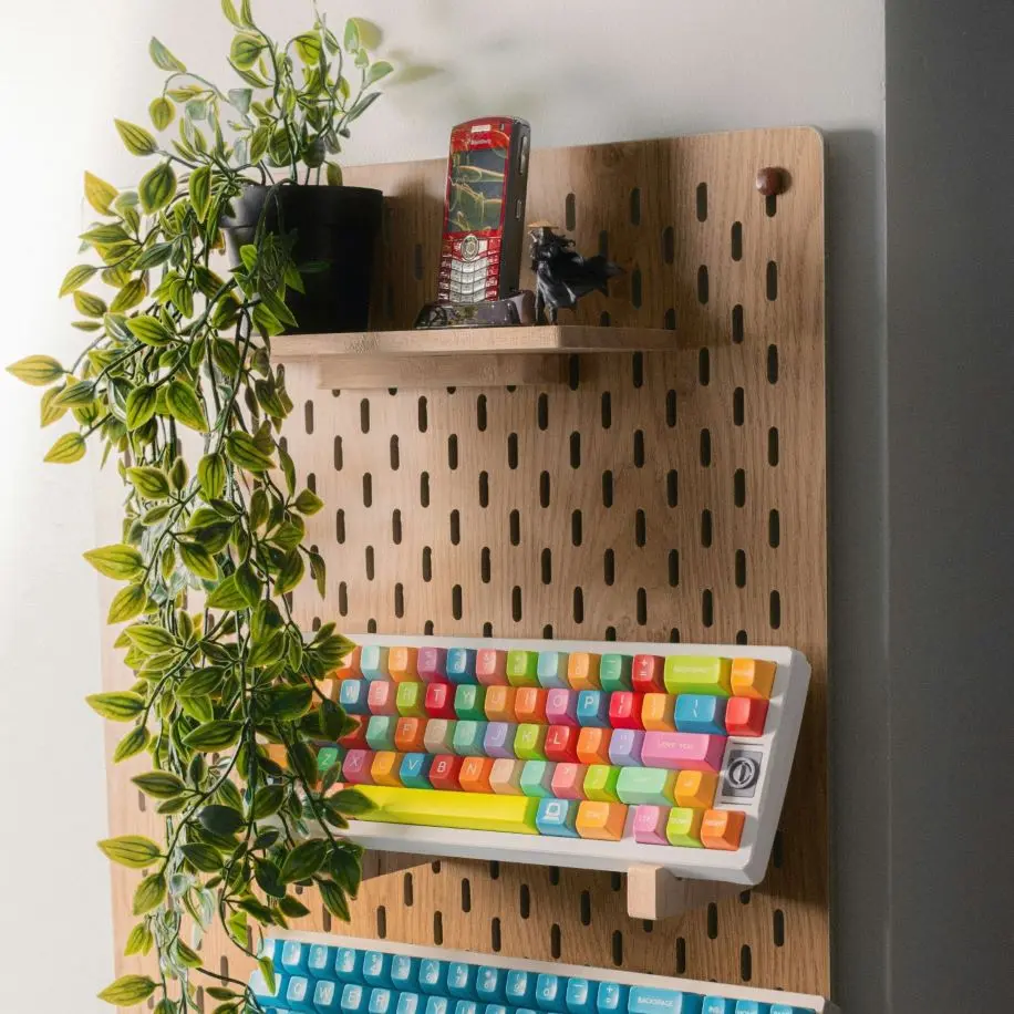 Pannello forato in legno con ripiani utilizzato per organizzare una tastiera, una pianta e piccoli oggetti decorativi