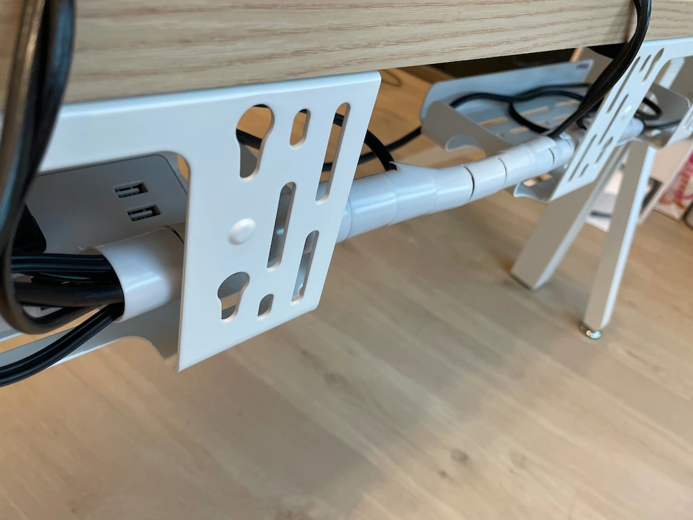 Under-desk cable management setup with a white cable sleeve keeping wires organized beneath a Revon standing desk.