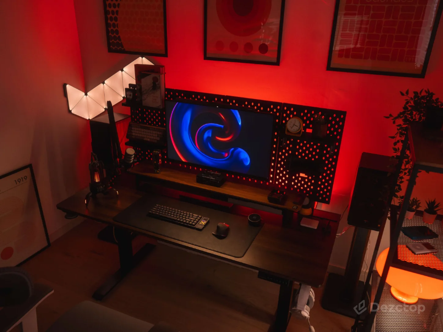Gaming setup with a Bifrost Elite standing desk, red RGB lighting, a wide monitor, illuminated wall panels, and organized desk accessories.