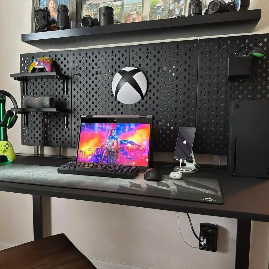 Postazione gaming con pannello forato nero da parete Dezctop, utilizzato per organizzare accessori, console e dispositivi sulla scrivania.