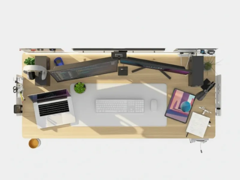 Top-down view of a clean and organized workspace with dual monitors, a laptop, keyboard, mouse, and accessories arranged on Revon standing desk.