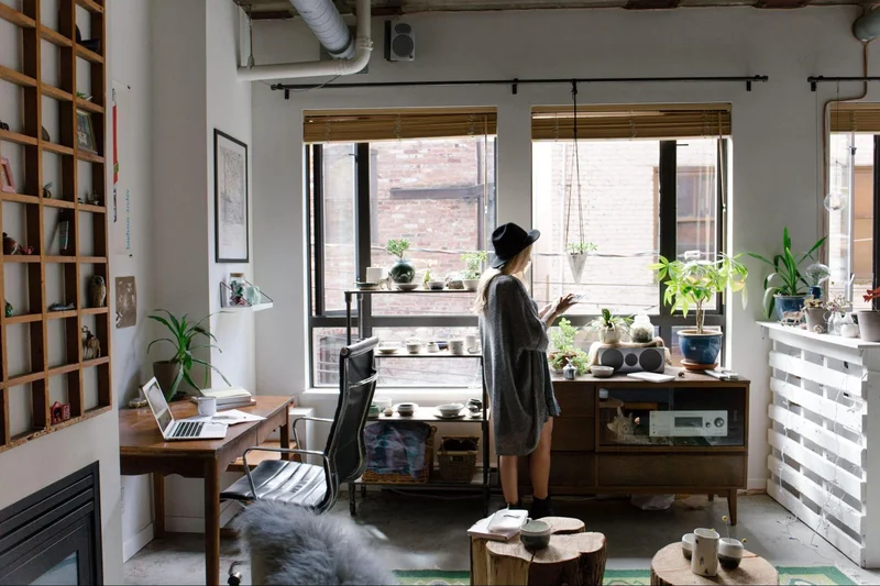 a woman standing in front of a window in a room filled with plants, creating a stylish home office setup.