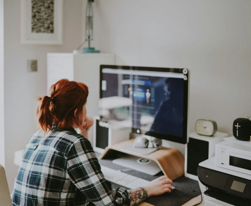 A woman sitting at a desk with a computer and a monitor, creating a productive home office setup.
